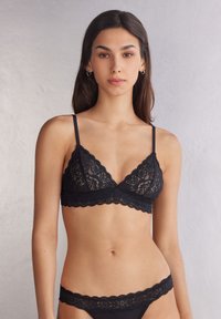 Zwarte kanten bralette met geschulpte randen, driehoekige cups en verstelbare bandjes. Gecombineerd met een bijpassende bikinibroek met kantafwerking.