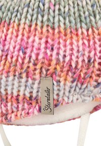 Close-up of multicolored chunky knit fabric with a beige tag labeled "Sterntaler" and part of white fleece lining visible.