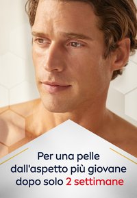 Primo piano del viso di un uomo con pelle liscia e leggermente abbronzata, capelli corti e mossi, colore naturale delle labbra e uno sfondo neutro che mette in risalto la texture della pelle.