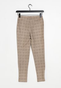 Pantalons à carreaux beiges sur un cintre noir, présentant une coupe ajustée et une texture lisse, avec une taille mi-haute et des jambes fuselées.