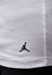 White ribbed fabric t-shirt featuring a small black Jordan logo near the hem, with visible stitching accents and a fitted design.
