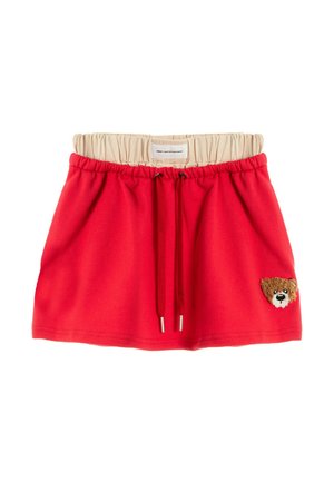 Falda roja con cordón, cintura elástica beige y un pequeño parche con la cara de un oso de peluche en la parte inferior derecha.