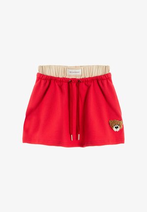 Falda roja con cordón, cintura elástica beige y un pequeño parche con la cara de un oso de peluche en la parte inferior derecha.
