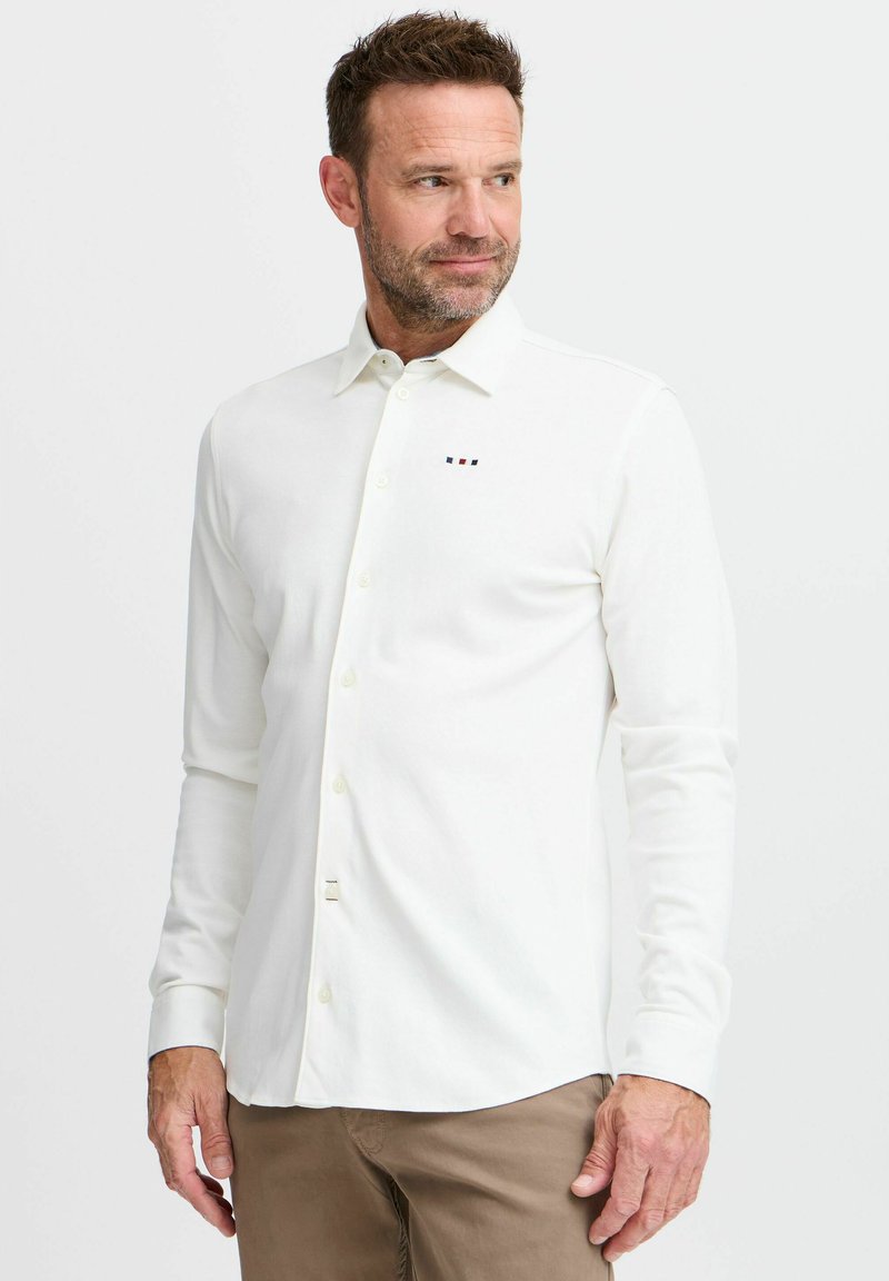 Cămașă albă cu mânecă lungă, cu nasturi, cu un design subtil pe piept ce include dungi colorate mici; textură fină și guler clasic.