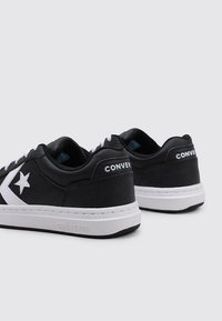 Adidași negri din piele cu logo alb în formă de stea, accente albe, design cu șireturi și o talpă din cauciuc texturat. Construcție minimalistă.