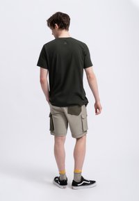 Donkergroene T-shirt met korte mouwen, relaxte pasvorm, gecombineerd met lichtbeige cargoshorts met zakken, zwarte sneakers en sokken met gele accenten.