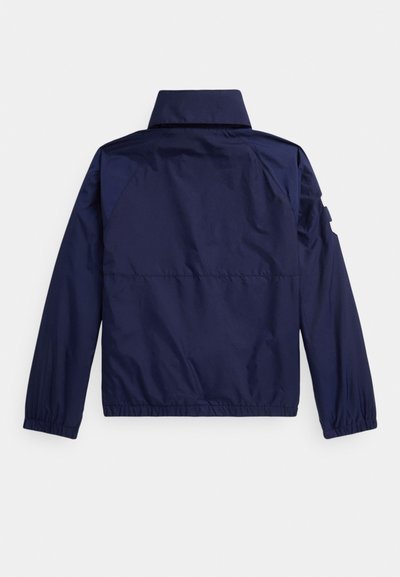 Casaco leve azul-marinho com mangas compridas, punhos elásticos e gola alta reta, visto pelas costas.