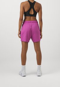Sostén deportivo negro con un diseño de espalda recortada, combinado con pantalones cortos deportivos rosas que cuentan con una cinturilla elástica y una textura suave.