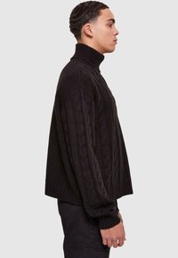 Maglione a collo alto lavorato a maglia nero con maniche lunghe, caratterizzato da una texture strutturata e un design cropped. Vista laterale con polsini a coste.