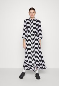 Vestido longo com padrão de ondas em preto e branco, com frente abotoada e mangas até ao cotovelo, combinado com ténis pretos.