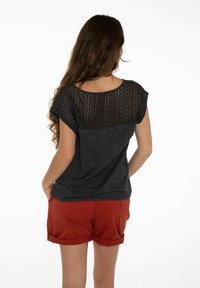 Svart topp med kort ärm och spetsbakstycke, tillsammans med röda korta byxor. Toppen har rund halsringning och slapp passform.