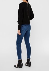 Camiseta negra de manga larga con cremallera en la parte posterior, combinada con jeans ajustados de color azul oscuro y botas negras hasta el tobillo con acentos blancos.