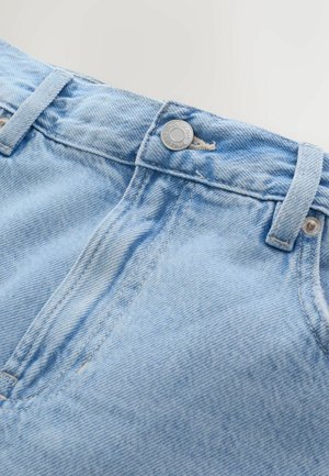 Detailný záber svetlomodrých riflí z denimu zobrazujúci pás, kovové gombíky, očká na opasok a švy na prednom vrecku na jednoduchom pozadí.