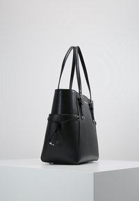 Zwarte leren tote bag met twee handvatten, een gestructureerd ontwerp, een getextureerde oppervlakte en een voorvak met een trekkoordsluiting.