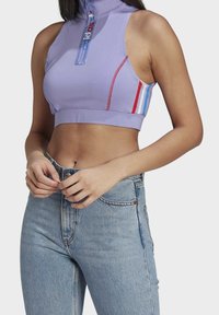 Lila kortärmad träningströja med hög krage och blixtlås. Har röda och blå ränder på sidorna, tillverkad i stretchig tyg. Kombineras med ljusblå jeans.