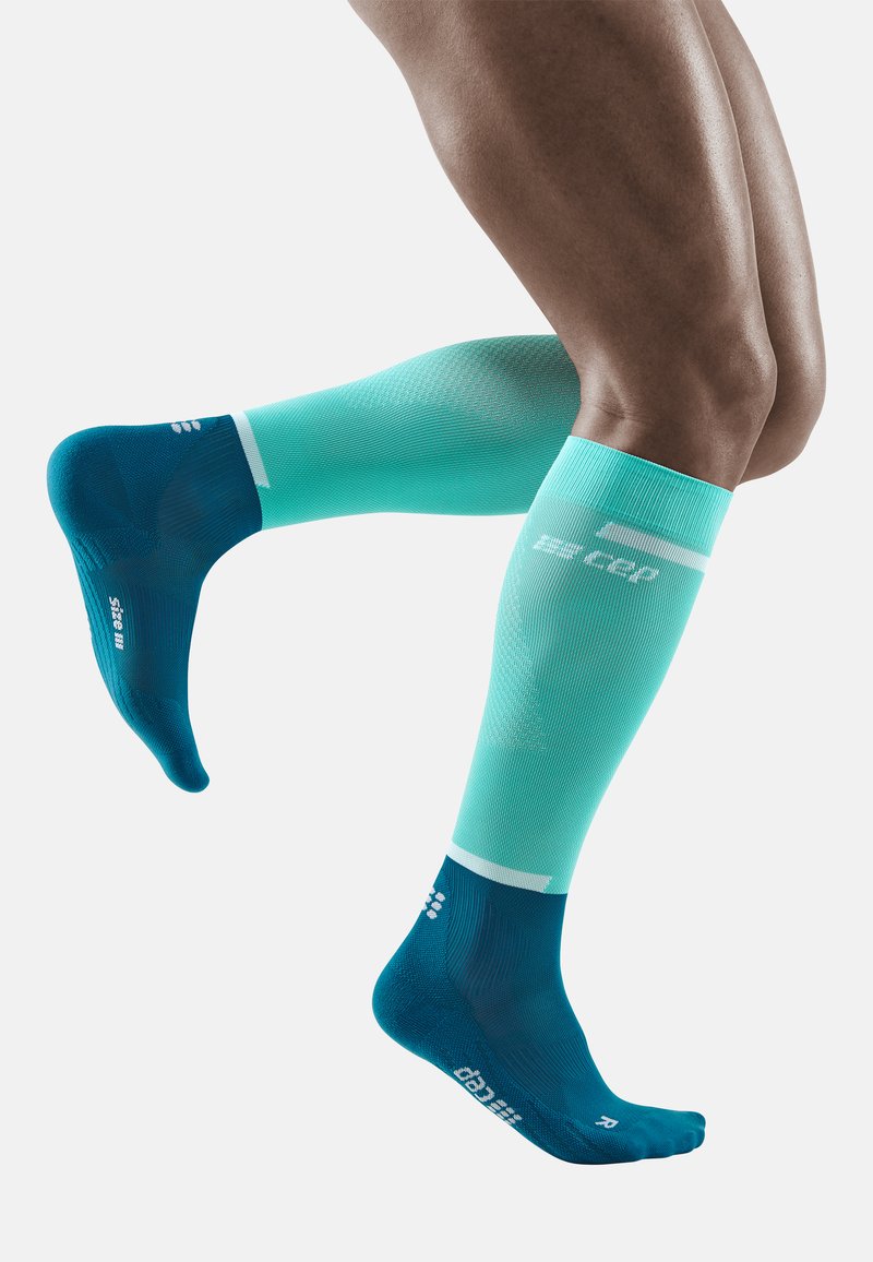 Compressiekousen in blauw en aqua met een textuurpatroon, voorzien van enkelondersteuning en verstevigde tenen, ontworpen voor atletisch gebruik.