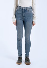 Jeans de denim azul de talle alto con un ajuste slim, con herrajes en tono cobre, bolsillos frontales y una textura desgastada para un look casual.
