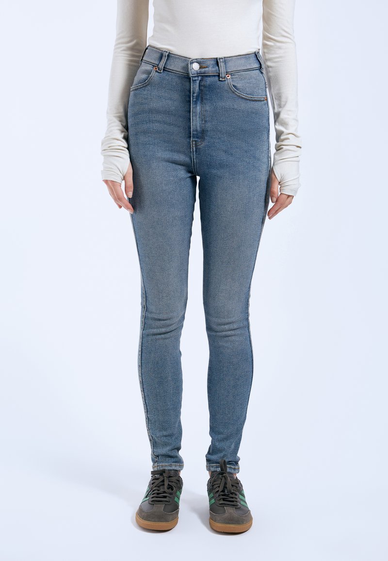 Jeans de denim azul de talle alto con un ajuste slim, con herrajes en tono cobre, bolsillos frontales y una textura desgastada para un look casual.