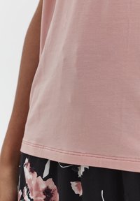 Top di cotone rosa con una consistenza liscia, dotato di orlo dritto e maniche corte, abbinato a una gonna stampata floreale in colori scuri.