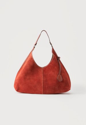 Sac à épaule en daim marron doux et épais avec une seule bandoulière, une couture décorative le long du bord supérieur et un gland en cuir sur le côté.