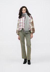 Károvaná oversized bunda v krémovej, hnedej a ružovej farbe, vrstvená cez ružový top, kombinovaná s olivovo zelenými nohavicami s rovnými nohavicami a sivým šálom. Čierne čižmy.