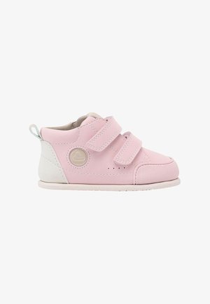 Zapato rosa para niño pequeño con talón blanco, dos correas de velcro, suela beige y logotipo circular en el costado.