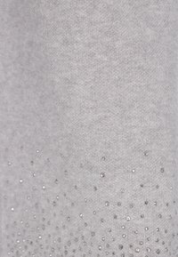 Šedá látka s hladkou texturou, na které jsou rozptýlené stříbrné flitry vytvářející gradientový efekt směrem k dolní části.