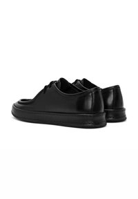 Zapatos de cuero negro con punta redondeada, cierre de cordones y suela de goma texturizada. El diseño presenta acentos lisos y brillantes.