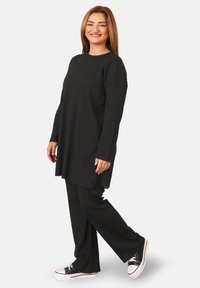 Tunic nera a coste con maniche lunghe, abbinata a pantaloni neri a coste e sneakers nere con accenti bianchi. Tessuto liscio, vestibilità comoda.