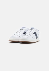 Zapatillas de cuero blancas con detalles en azul marino, punta perforada y cordones grises. Suela de goma con ribete marrón, que cuenta con un diseño de logo lateral.