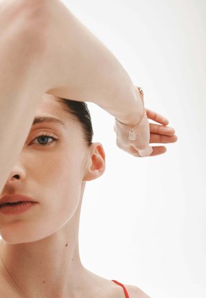 Pulsera delicada de cadena de oro con un charm rectangular, que presenta una superficie clara y un sutil grabado, llevada en una muñeca parcialmente visible.