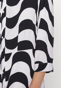 Camisa em preto e branco com padrão de ondas, fecho frontal com botões, mangas curtas, tecido texturizado e corte relaxado.