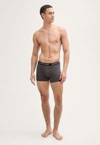 Dunkelgraue Boxer-Shorts aus Baumwolle, ausgestattet mit einem elastischen schwarzen Bund mit weißer Markenbezeichnung, figurbetontem Schnitt und glatter Textur.