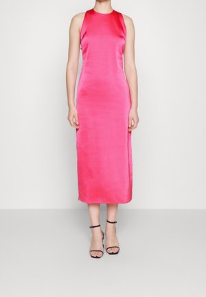 Femme portant une robe midi en satin rose vif sans manches avec des sandales à talons hauts noires à bride à la cheville sur un fond uni.