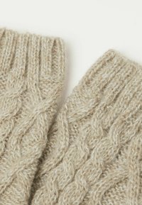 Beige strikkede fingerløse handsker lavet af blød uld, med et tekstureret kabelmønster og ribbet manchet for ekstra varme.