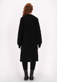 Zwarte lange cardigan van gebreid materiaal, met een relaxte pasvorm, verlaagde schouders en een verticale naad op de achterkant.