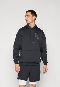 Mørkegrå hoodie med en forlommer, snoretræk i hætten og UA-logo. Parret med sorte shorts og en hvid atletisk undertrøje.