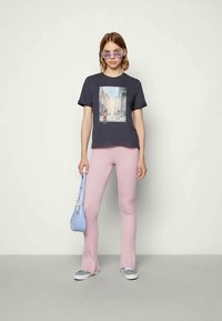 T-shirt azul-marinho com impressão fotográfica, combinado com calças rosa em boca de sino com nervuras. Os acessórios incluem uma mala azul-clara e óculos de sol roxos.