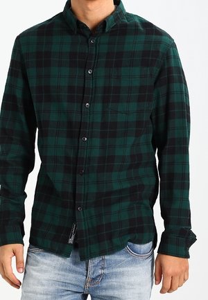 Chemise en flanelle verte et noire avec un col à patte boutonnée, des manches longues, une poche avant et un motif à carreaux. Fabriquée en tissu doux.