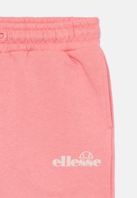 Rosa joggebukser laget av mykt stoff, med elastisk midje, sidelommer og en hvit "ellesse" logo på benet.