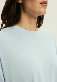 Jasnoniebieska bluza z okrągłym dekoltem, wykonana z miękkiego materiału. Posiada subtelne wytłoczone logo z przodu oraz luźny krój.