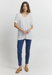Hvid kortærmet bluse med v-hals og samlede detaljer, parret med blå slim-fit jeans og brune loafers. Enkel og afslappet design.