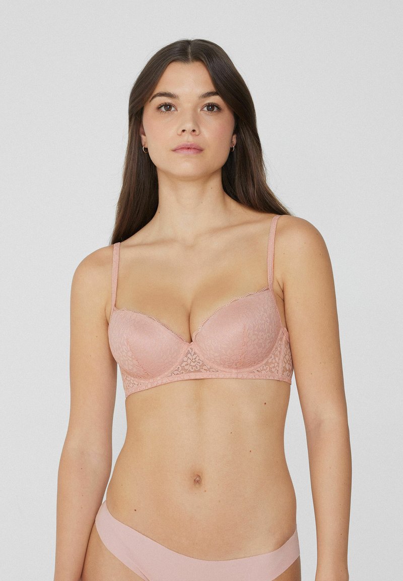 Svetle růžová krajková podprsenka s kosticemi, hladkými košíčky, nastavitelnými ramínky, vlnkovanými okraji a strukturovaným vzorem. Navržena pro podporu a pohodlí.