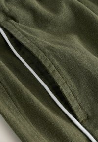 Gros plan sur un tissu vert olive avec un cordon de serrage blanc et un détail de couture froncée.