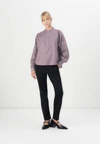 Randig blus med hög krage, knappslå och puffärmar, tillsammans med figursydda svarta byxor och svarta klackskor.