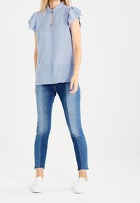 Modrá a bílá pruhovaná blůza s volánkovými rukávy, s výstřihem ve tvaru klíčové dírky, v kombinaci s tmavě modrými skinny dž íny a bílými teniskami.