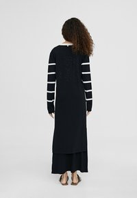 Abito lungo nero a maniche lunghe con righe bianche, dotato di un dettaglio logo rotondo sulla parte posteriore e una vestibilità rilassata. Materiale in cotone morbido.