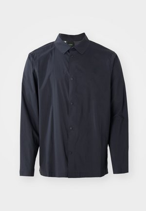 Marineblå skjorte med knappestolpe, krage, lange ermer og teksturert stoff. Har en frontplacket med knapper og en subtil logo-detalj.