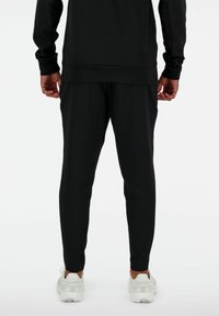 Pantaloni da jogging neri e atletici con una vestibilità aderente, vita elastica e polsini a coste. Indossati con sneakers bianche, mostrando una texture liscia e opaca.