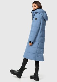 Abrigo largo tipo puff en azul claro con capucha, que presenta secciones acolchadas, un parche con el logo en el hombro izquierdo y bolsillos laterales.